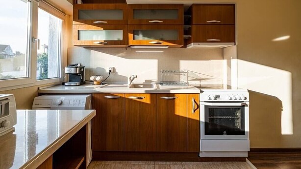 A modern kitchen with wooden cabinets, a built-in oven, a sink, and a window providing natural light. - Primorski 2bdrm Central Apartment (Varna)