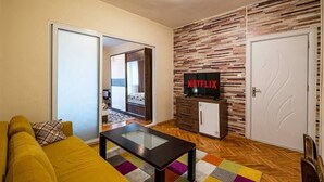 A living room with a sofa, a coffee table, a TV on a cabinet, and a patterned rug. - Primorski 2bdrm Central Apartment (Varna)