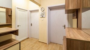 A hallway with two white doors, a clock, and a small floral artwork on the wall. - Primorski 2bdrm Central Apartment (Varna)