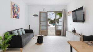 Una sala de estar moderna con un sofá, una mesa de centro, un televisor y una puerta que da a un espacio al aire libre.
