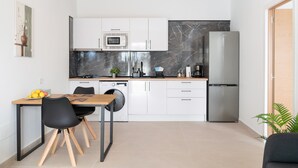 Una cocina moderna con armarios blancos, un salpicadero de mármol, un refrigerador de acero inoxidable y una zona de comedor con una mesa y sillas.