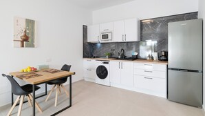 Una cocina moderna con armarios blancos, un refrigerador de acero inoxidable, un microondas y una lavadora.