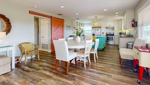 Une cuisine moderne avec des meubles blancs, une porte rouge et un coin repas comprenant des chaises blanches et une table en bois.