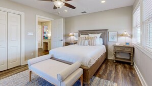 Une chambre à coucher avec un grand lit, un ventilateur de plafond, une table de chevet avec des lampes et une fenêtre avec des stores.