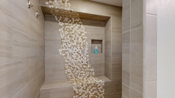 Une salle de bain dotée d’un mur décoré d’une mosaïque originale et d’une petite étagère sur laquelle se trouve une bouteille.