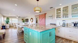 Une cuisine spacieuse avec des meubles de couleur turquoise, un plan de travail en granit et un luminaire suspendu.