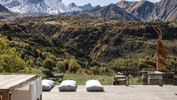 A wooden deck with lounge chairs and pillows, overlooking a mountainous landscape with a sculpture. - Chalet d’Albiez: 360° Mountain Views and Panoramic Terrace (Albiez-Montrond)