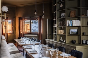 Uma sala de jantar com uma mesa comprida posta para seis pessoas, uma estante de livros e vista para uma paisagem coberta de neve.