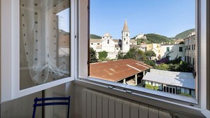A room with a window overlooking a town, a radiator, and a blue chair. - Apartment 'Il Borgo Incantato with Garage' with Wi-Fi and Air Conditioning (Finale Ligure)