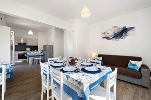 A dining area with a table set for four, a brown sofa, and a kitchen in the background. - Apartment 'Il Borgo Incantato con garage' with Wi-Fi and Air Conditioning (Finale Ligure)