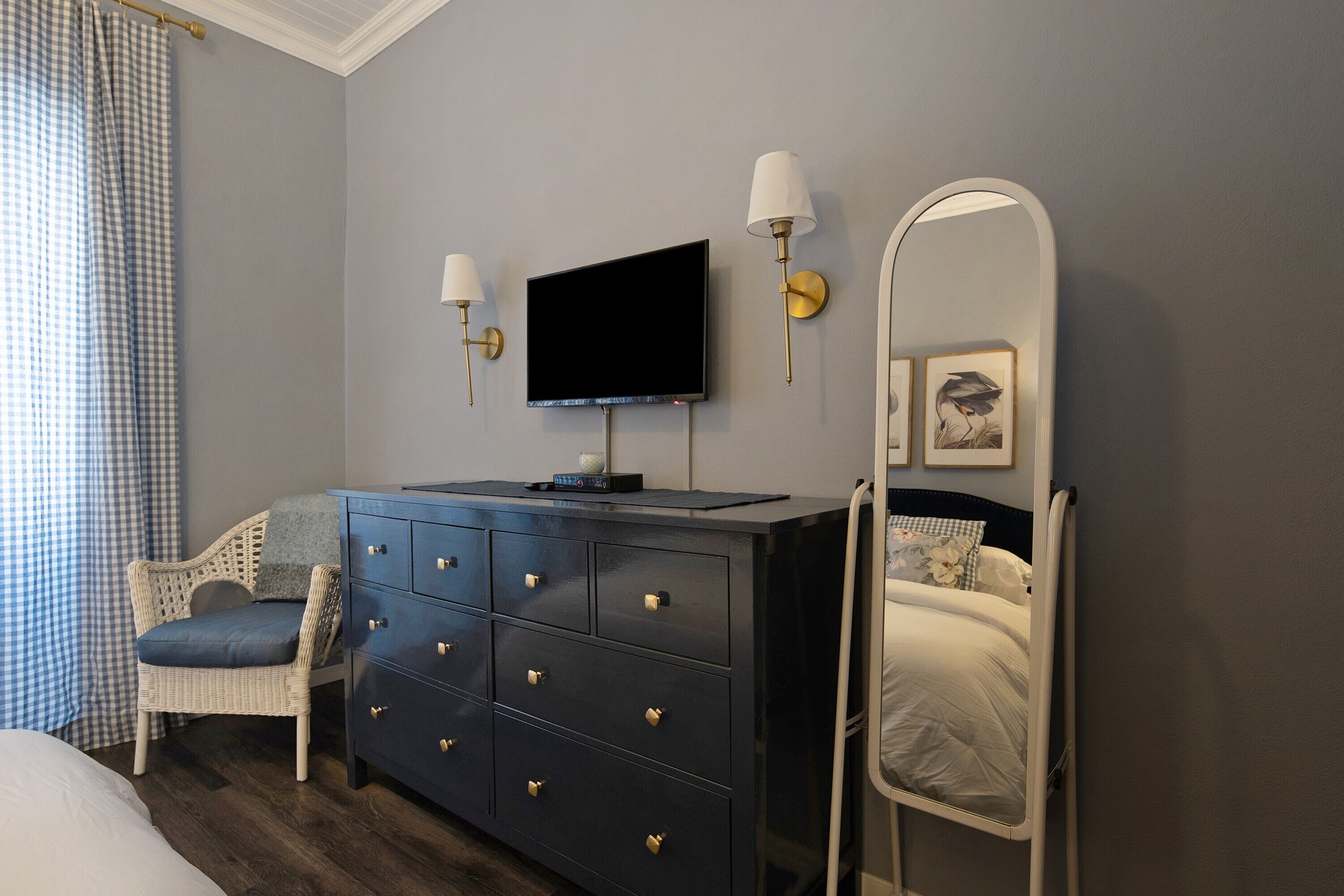 A bedroom with a bed, a dresser, a television, a mirror, and a chair.