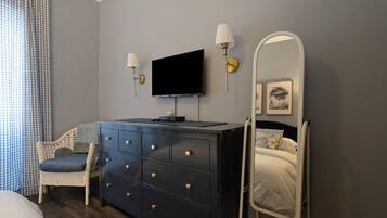A bedroom with a bed, a dresser, a television, a mirror, and a chair.