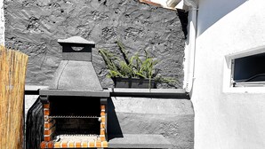 Une terrasse avec un barbecue, un pot de fleurs et un mur en pierre.