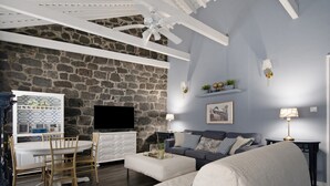 Un salon avec un mur en pierre, un téléviseur à écran plat, une table à manger avec des chaises, un canapé et un ventilateur de plafond.
