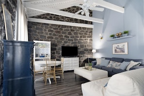 A living room with a stone wall, a flat-screen TV, a white dining table with chairs, a sofa, and a ceiling fan.