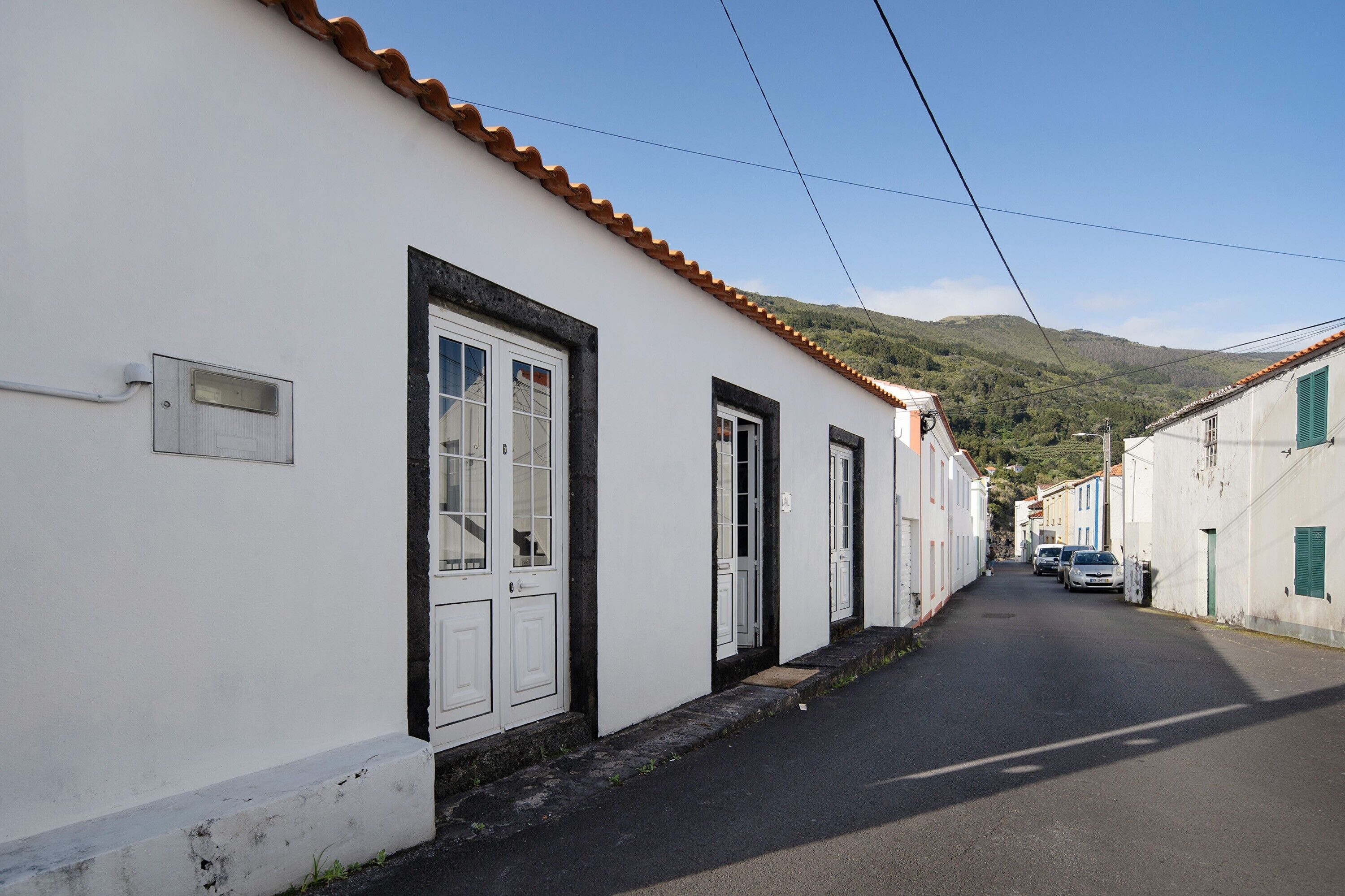 A narrow street with white buildings, a tiled roof, and a mountain in the background.