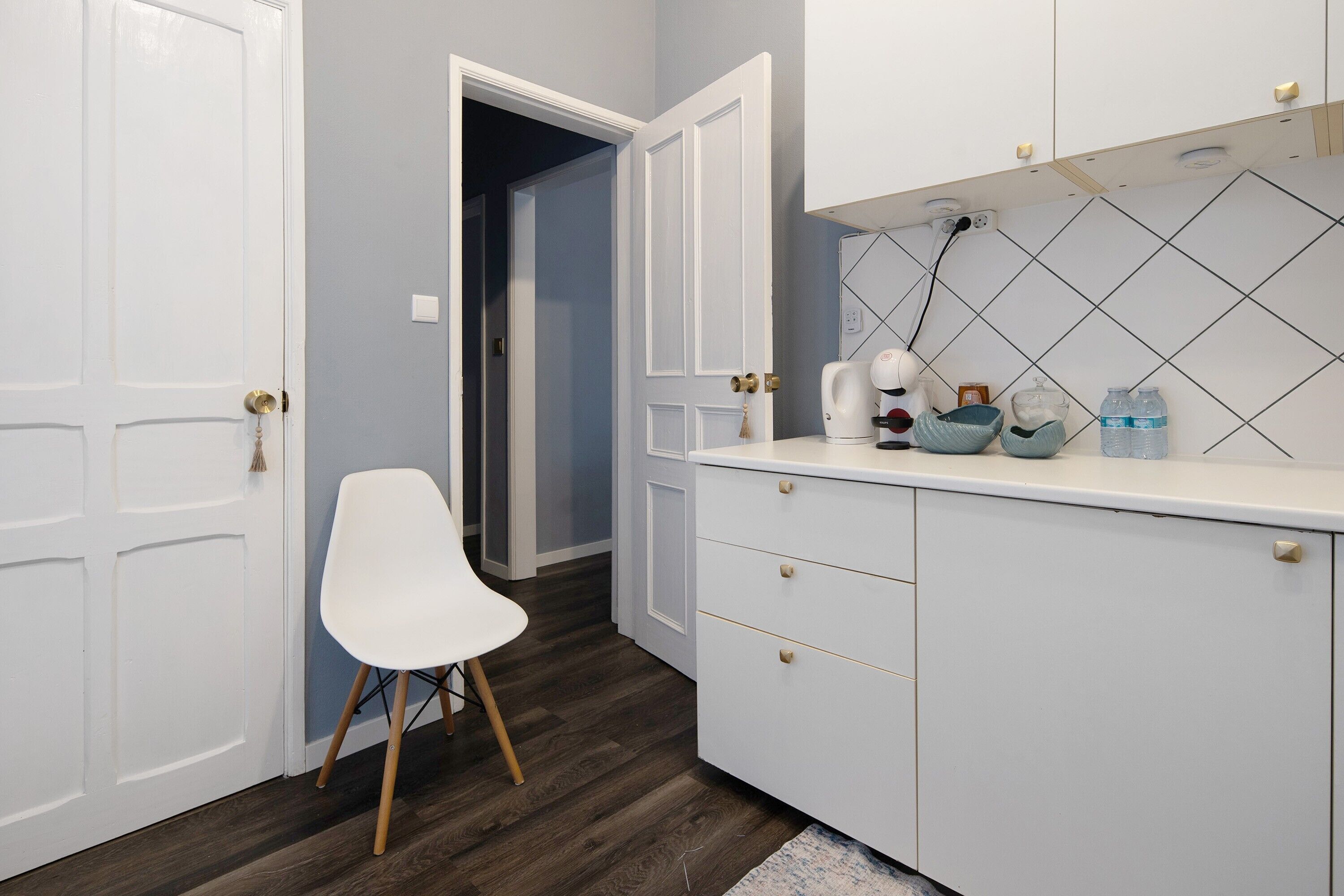 Una cocina moderna con armarios blancos, una silla blanca y salpicadero de azulejos.