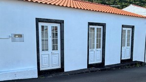 Un bâtiment blanc avec un toit recouvert de tuiles rouges, deux portes blanches et une petite fenêtre sur le côté.