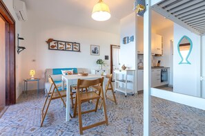 Un accogliente soggiorno con divano, tavolo da pranzo e sedie, una cucina con mobili bianchi e un pavimento piastrellato.