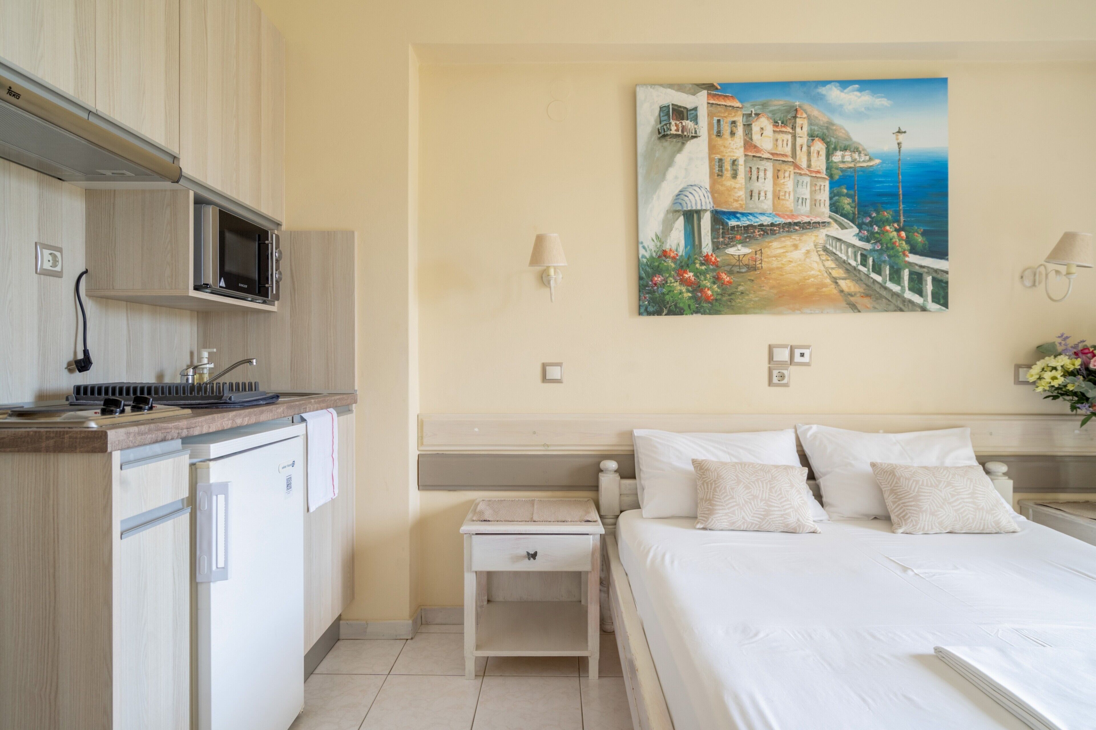 Una habitación de hotel con cama, mesita de noche, microondas, un mueble pequeño y un cuadro en la pared.