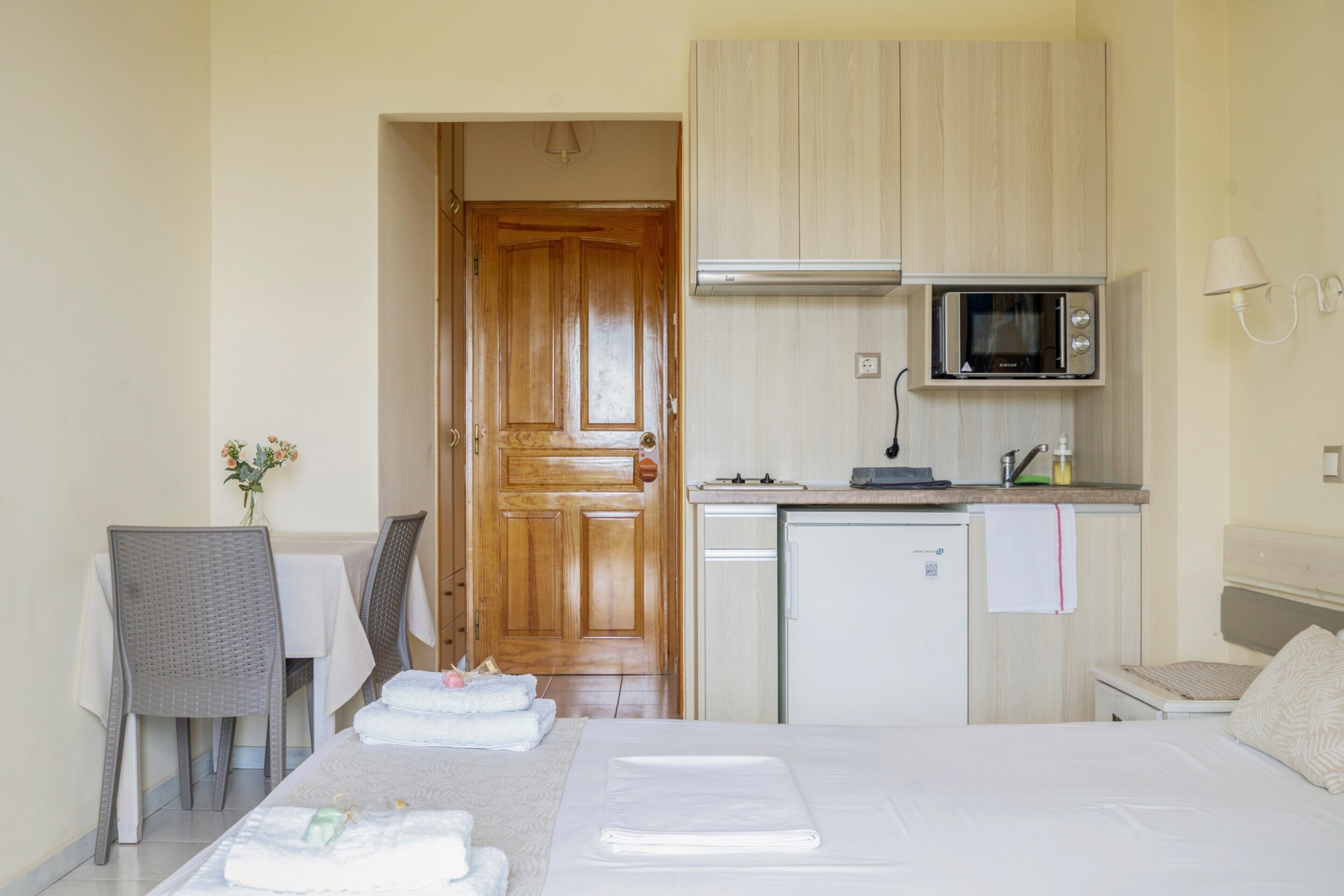 A hotel room with a bed, a dining table with chairs, a kitchenette with a microwave, and a wooden door.