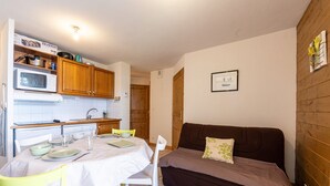 A compact kitchen with a microwave, wooden cabinets, and a dining table set for four. - Apartment 'Ty Aravis' with Mountain View and Balcony (La Giettaz)