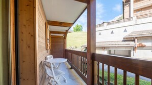 A wooden balcony with a table and chairs, overlooking a building with a sloped roof. - Apartment 'Ty Aravis' with Mountain View and Balcony (La Giettaz)