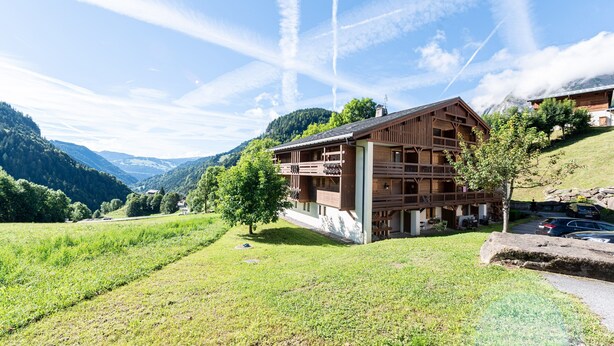 A wooden chalet with a balcony, surrounded by green fields and mountains. - Apartment 'Ty Aravis' with Mountain View and Balcony (La Giettaz)