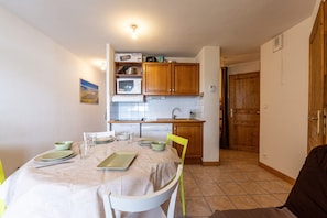 Una cocina compacta con armarios de madera, microondas y una mesa de comedor preparada para cuatro comensales.