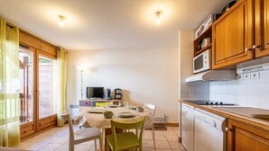 A kitchen with wooden cabinets, a stove, a microwave, and a dining area with chairs and a table. - Apartment 'Ty Aravis' with Mountain View and Balcony (La Giettaz)