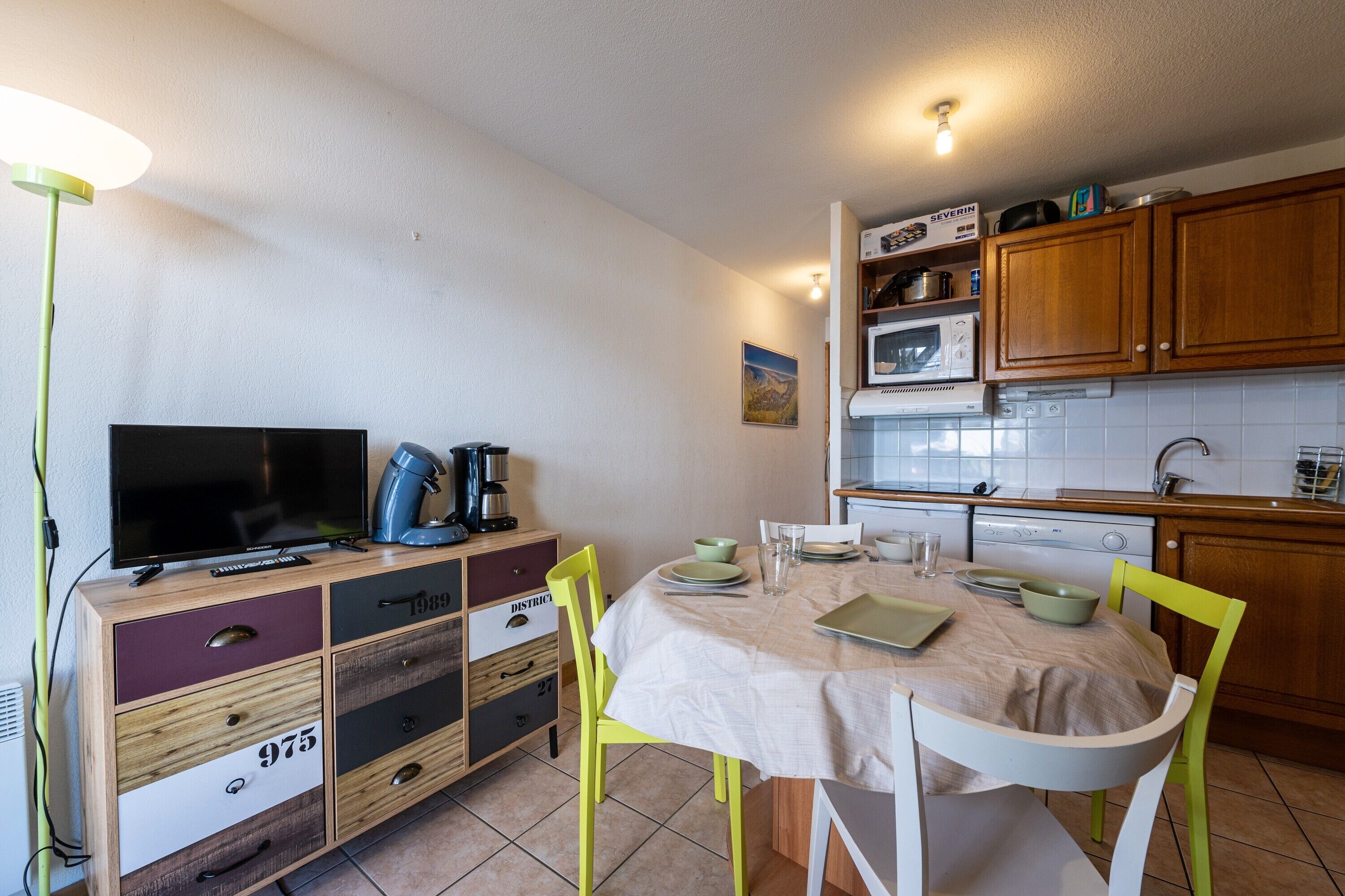 Une cuisine de taille réduite comprenant une table à manger, des chaises, un téléviseur et un four à micro-ondes.