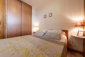 Un dormitorio con cama, armario de madera, lámparas de noche y cuadros en la pared.