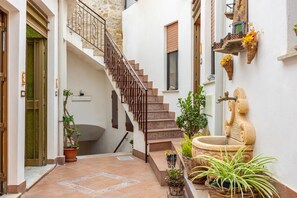 Un pasillo estrecho con una escalera, plantas en macetas y una fuente de piedra.