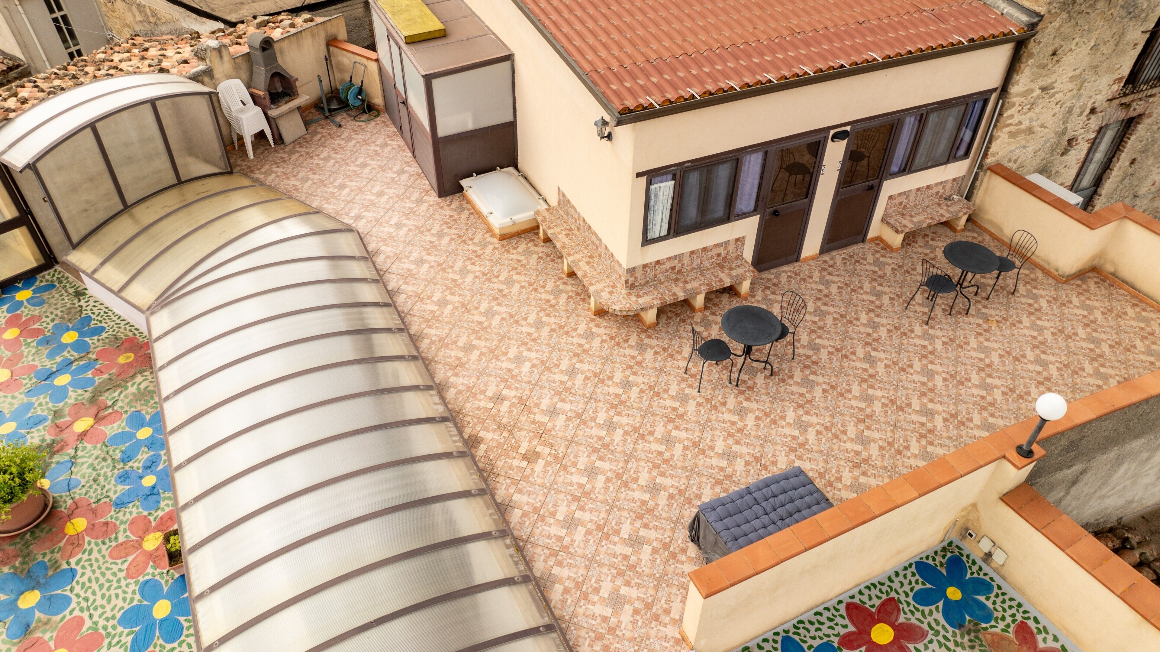 Eine Dachterrasse mit gebogener Glasreling, einer kleinen Sitzecke mit Tisch und Stühlen sowie einem Blumentopf.