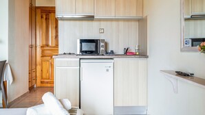 Una cocina compacta con microondas, un refrigerador pequeño, armarios de madera y una lámpara colgante.
