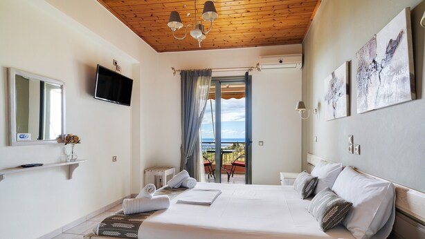 Un dormitorio con cama, televisor, balcón con mesa y sillas, y obras de arte en la pared.