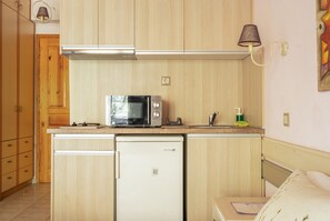 Una cocina compacta con armarios de madera, un microondas, un refrigerador pequeño y una lámpara de pared.
