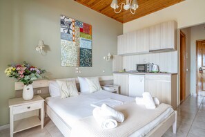 Quarto com cama, mesas de cabeceira, um vaso de flores, um quadro e uma kitchenette.