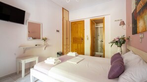 A hotel room with a bed, a television, a mirror, a small table, and a shower area. - Studio Apartment 'Nontas Home 24' with Mountain View, Wi-Fi and Air Conditioning (Kalamitsi)