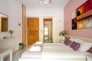 A hotel room with a bed, a mirror, a wooden door, a shower, and a wall with a colorful painting. - Studio Apartment 'Nontas Home 24' with Mountain View, Wi-Fi and Air Conditioning (Kalamitsi)