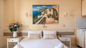 A hotel room with a bed, two nightstands, a vase of flowers, a painting of a coastal scene, and a view of the sea. - Studio Apartment 'Nontas Home 21' with Sea View, Wi-Fi and Air Conditioning (Kalamitsi)