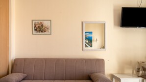 A beige sofa with two cushions, a small white table, and two framed artworks on the wall. - Studio Apartment 'Nontas Home 21' with Sea View, Wi-Fi and Air Conditioning (Kalamitsi)