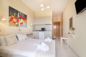Quarto de hotel com uma cama grande, um quadro na parede, uma cozinha compacta e uma televisão fixada na parede.