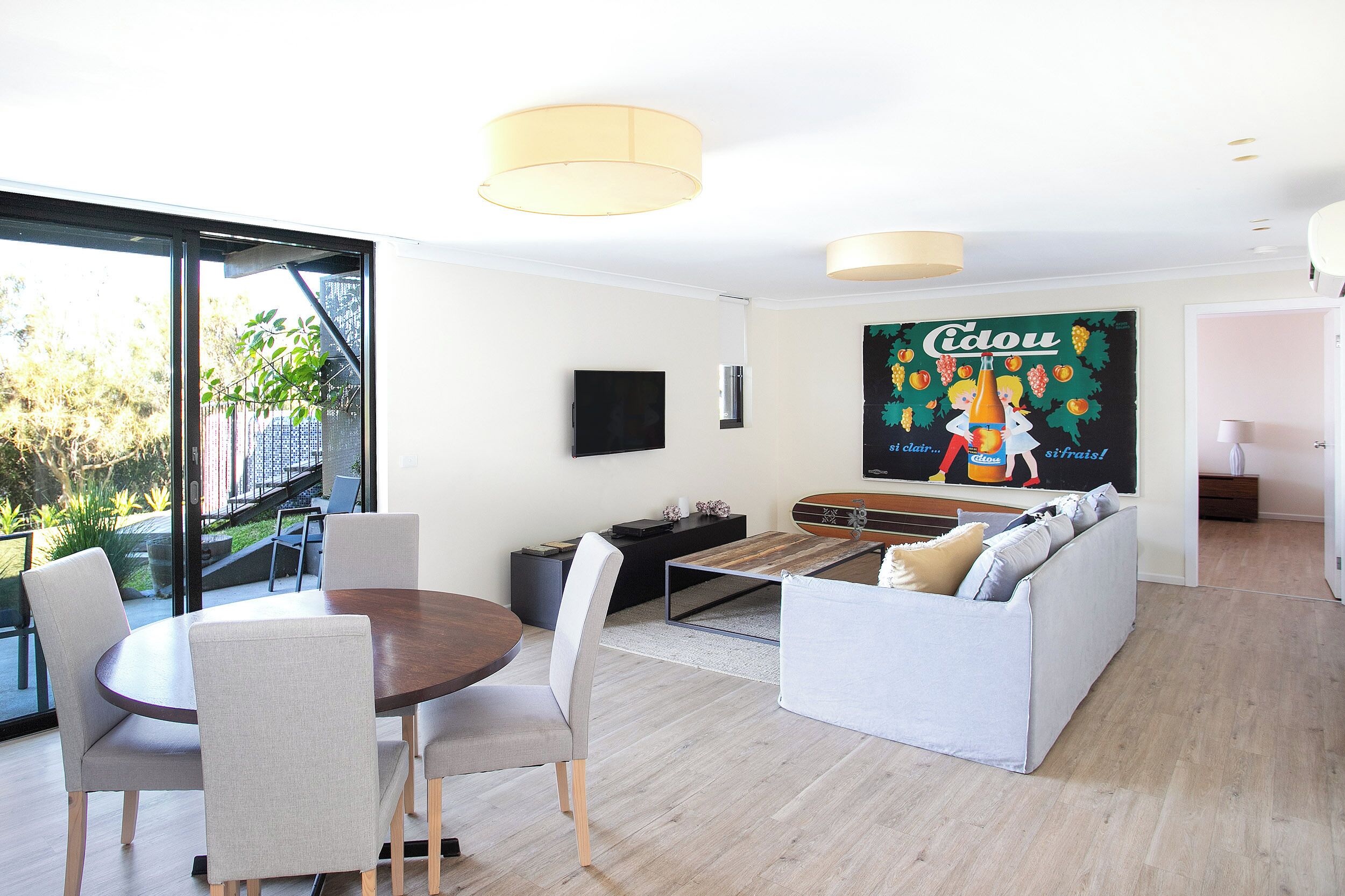 Un salon moderne comprenant un coin repas, un canapé et un téléviseur fixé au mur.