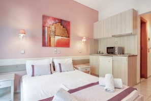 Quarto de hotel com cama, pequeno espaço de cozinha, um quadro na parede e duas luminárias.