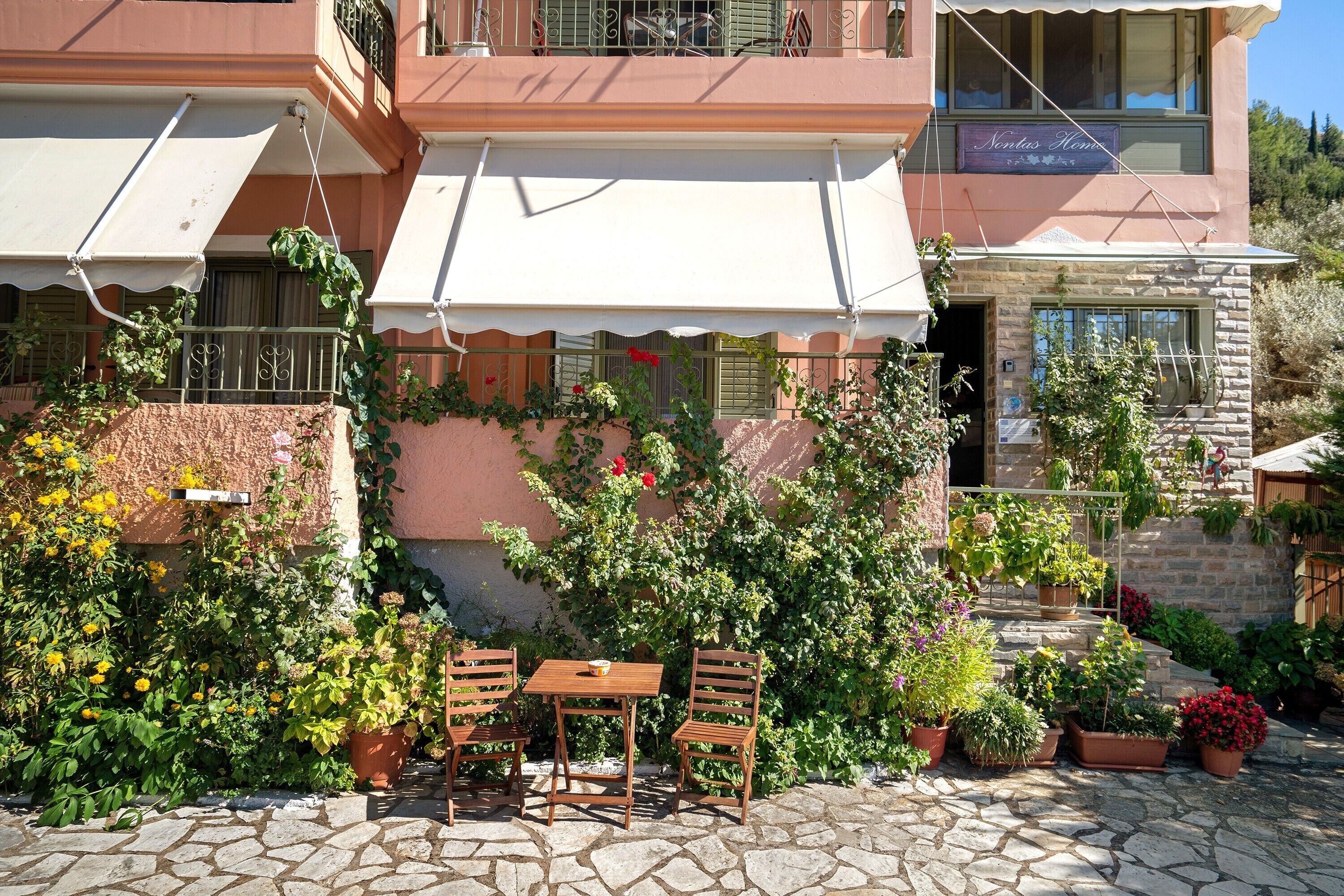 A courtyard with a table and chairs, surrounded by potted plants and a building with a balcony.