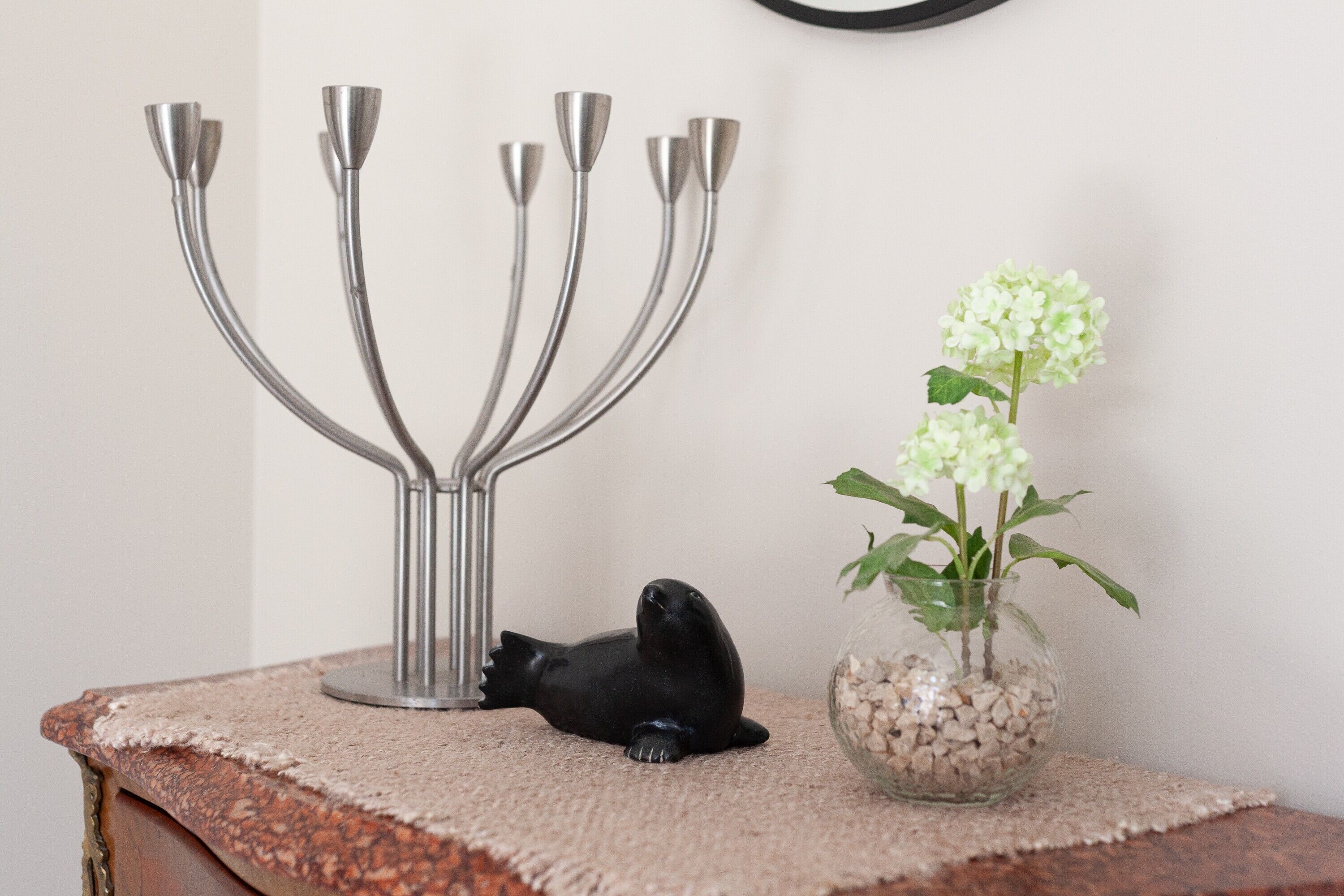 A decorative menorah, a black seal figurine, and a glass vase with white flowers on a textured surface.