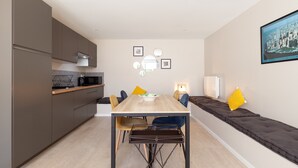 A modern kitchen with dark cabinets, a wooden table, and a seating area with cushions. - Apartment 'Havre De Paix' with Shared Pool, Private Terrace and Wi-Fi (Marseille)