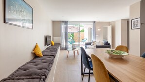 A modern living room with a sofa, a dining table, and a view through a glass door to an outdoor area. - Apartment 'Havre De Paix' with Shared Pool, Private Terrace and Wi-Fi (Marseille)