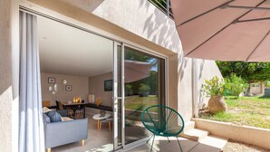 A modern outdoor living area with a sliding glass door leading to a dining space, a green chair, and a large umbrella. - Apartment 'Havre De Paix' with Shared Pool, Private Terrace and Wi-Fi (Marseille)